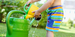 Kind gießt im Sommer Wasser in eine Gießkanne